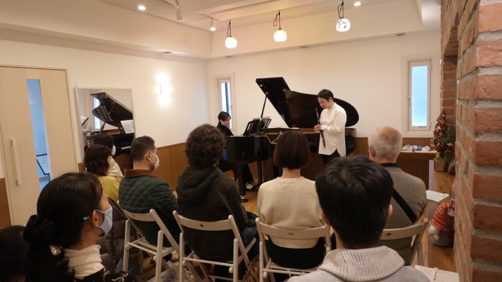 約20席の会場でフルートとピアノの演奏を聴く観客