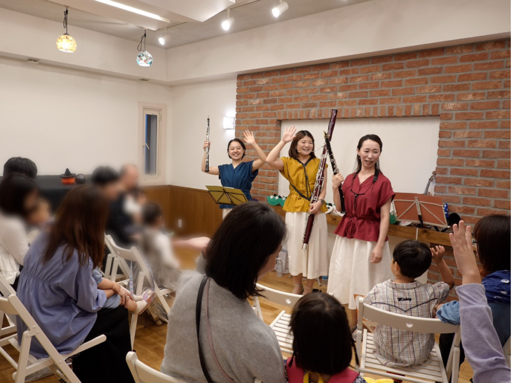 親子公演で、木管楽器の演奏者と客席の親子が一緒に手を上げている様子